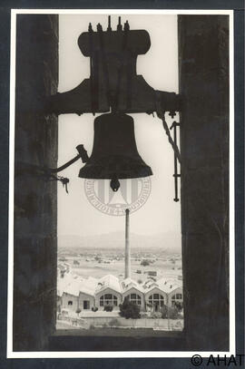 Primer pla de la campana de l'església parroquial de l'Assumpció amb la fàbrica tèxtil al fons.